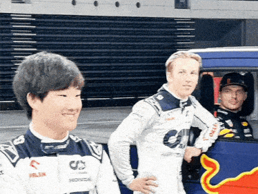 a group of racing drivers are standing next to each other in front of a red bull truck .