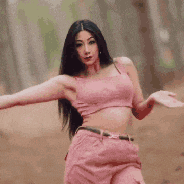 a woman in a pink top and pink shorts is dancing in the woods .