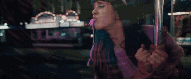 a woman with blue hair is blowing a bubble in a car window .