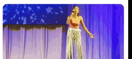 a woman is singing into a microphone on a stage in front of a blue curtain .