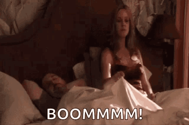 a woman is sitting on a bed next to a man and holding his penis .