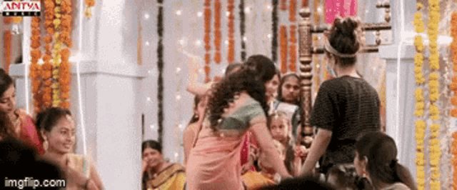 a group of women are dancing in a room with flowers hanging on the wall .