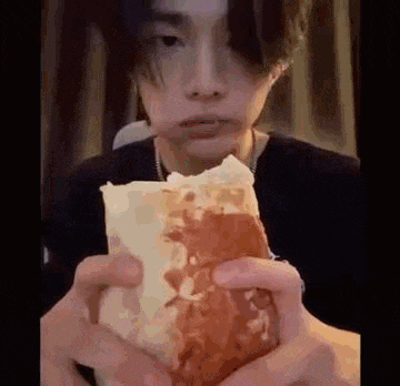 a young man is eating a large hamburger with a bite taken out of it .