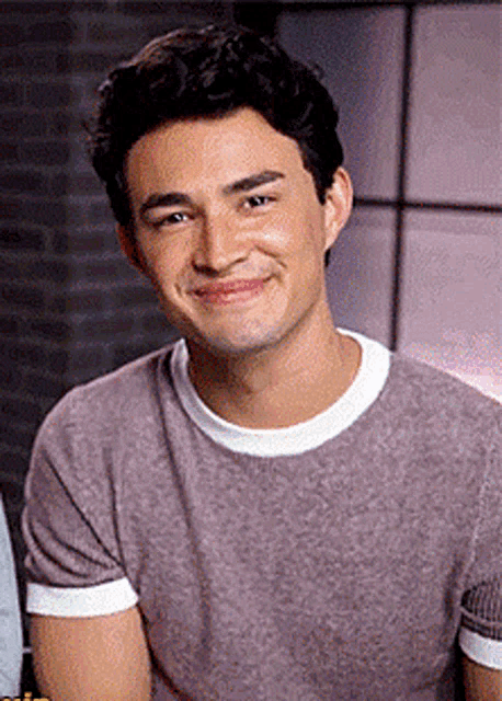 a young man is smiling and wearing a purple t-shirt .