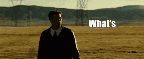 a man in a suit and tie is standing in a field with the words what 's written above him