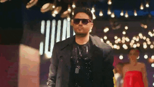 a man wearing sunglasses is walking down a runway in front of a group of people .