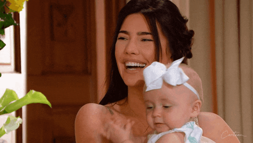 a woman is smiling while holding a baby with a white bow on her head