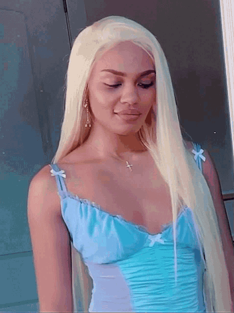 a woman with long blonde hair is wearing a blue dress and a cross necklace