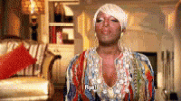 a woman in a colorful dress is standing in a living room and saying `` bye '' .