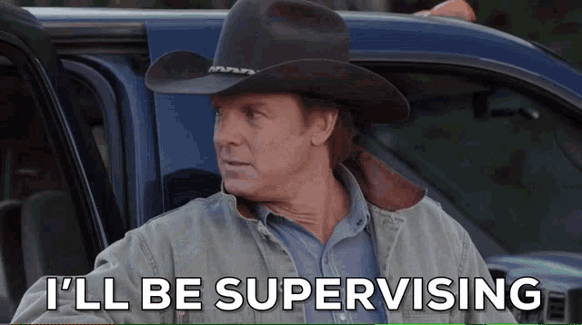 a man in a cowboy hat says i 'll be supervising in front of a blue truck