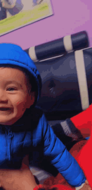 a baby wearing a blue jacket with a hood is smiling for the camera