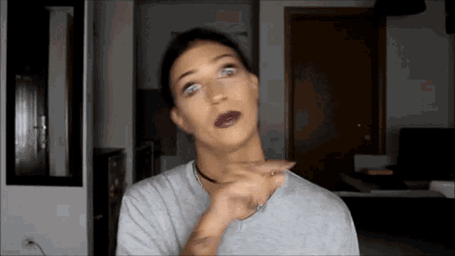 a woman wearing a choker and a gray shirt is making a funny face