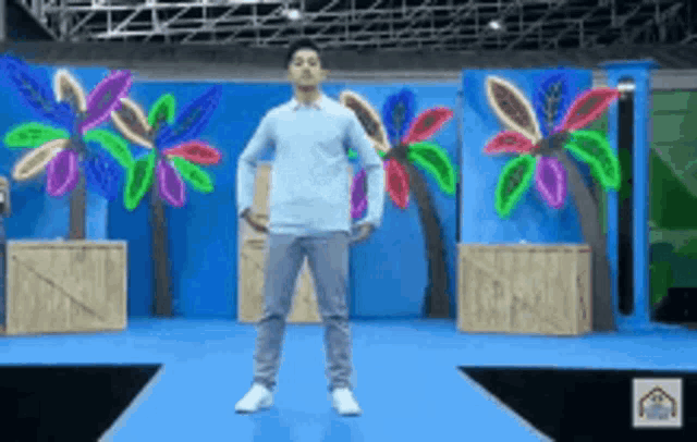 a man is standing on a runway in front of a blue background with palm trees and neon flowers .