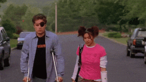 a man with a eye patch and crutches is walking down the street next to a woman .