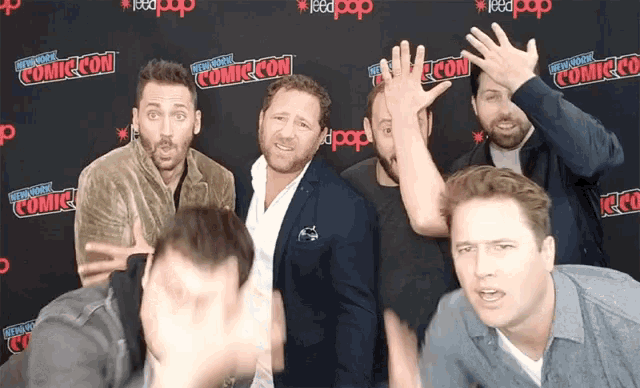 a group of men standing in front of a comic con backdrop