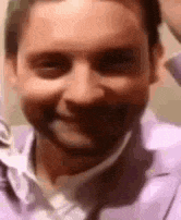 a close up of a man 's face with a beard wearing a purple shirt and tie .