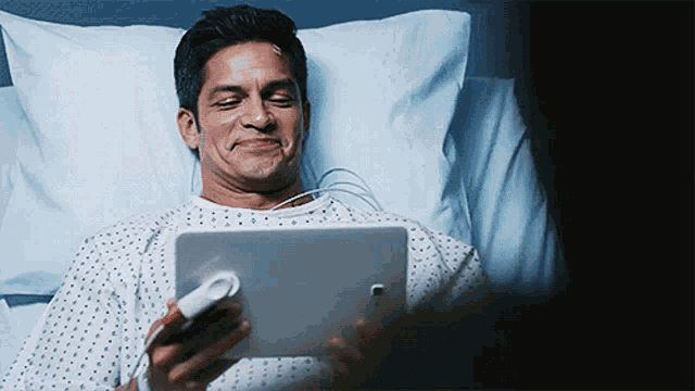 a man in a hospital gown is smiling while using a tablet
