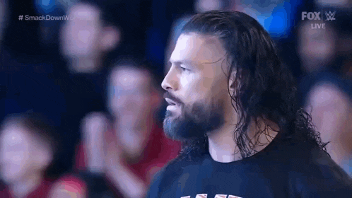a man with long hair and a beard is standing in front of a crowd in a stadium .
