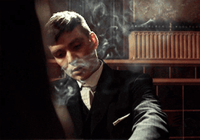 a man in a suit is smoking a cigarette in a dark room