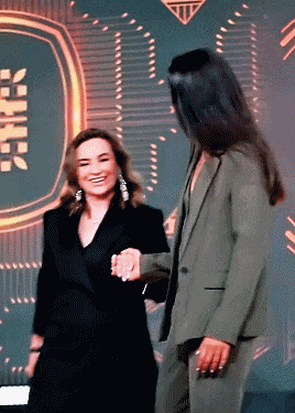 a woman in a green suit shakes hands with another woman in a black suit