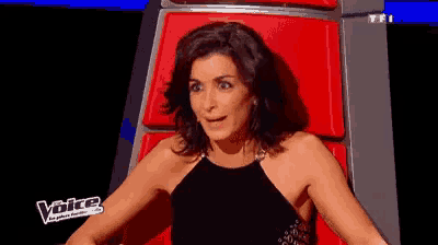 a woman in a black dress is sitting in a red chair with the word voice on it