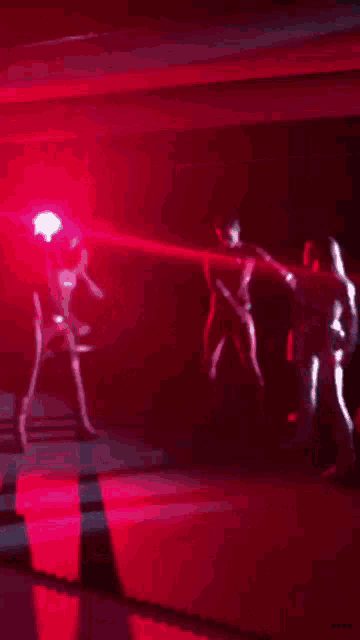 a group of people are dancing in a dark room with a red light shining on them