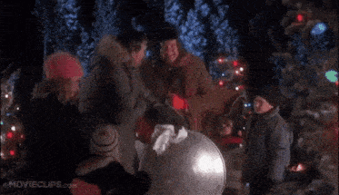 a group of people are standing around a christmas tree holding a bucket .