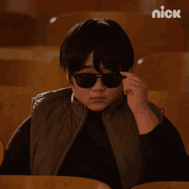 a young boy wearing sunglasses sits in a theatre with a nick logo in the background