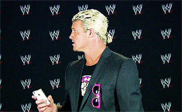 a man in a suit holds a cell phone in front of a wall with wrestlers logos on it