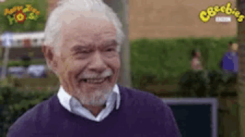 a man with gray hair and a beard is smiling in front of a bbc logo