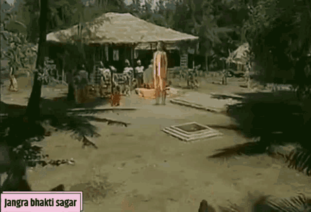 a man is standing in the dirt in front of a hut in a forest .