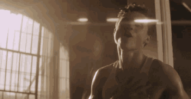 a man is standing in front of a window in a dark room with his hand on his chest .