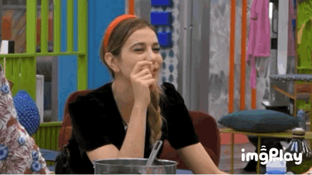 a woman is sitting at a table with a bowl of food and a spoon in her mouth .