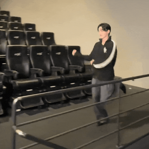 a man in a polo shirt is standing in front of a row of black seats in a theater