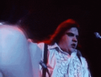 a man in a white shirt is singing into a microphone on stage .