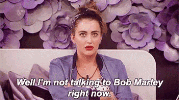 a woman is sitting on a bed with purple flowers in the background and talking to bob marley .