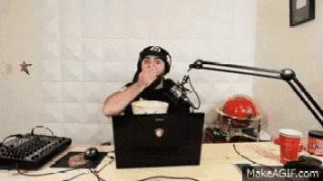a man is sitting at a desk with a laptop and eating popcorn .