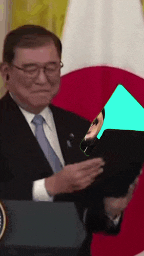 a man in a suit and tie sitting in front of a japanese flag