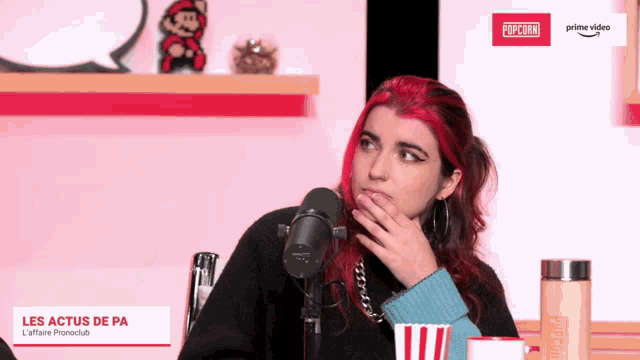 a woman with red hair is sitting in front of a microphone and a sign that says popcorn on it