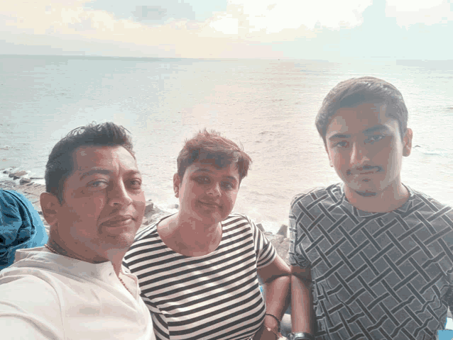 a man a woman and a boy pose for a picture with the ocean in the background