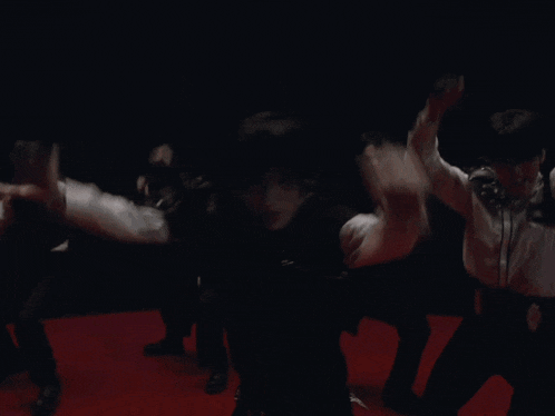 a group of men are dancing on a red carpet in a dark room