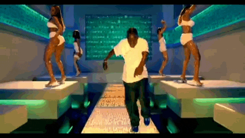 a man in a white shirt is dancing on a stage with three women in bikinis