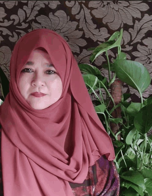 a woman wearing a red scarf stands in front of a plant