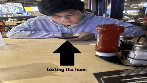 a man sits at a table with a ketchup bottle and a salt and pepper shaker and texting tha hoes