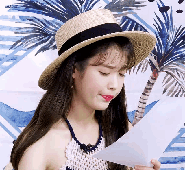 a woman wearing a straw hat is reading a piece of paper in front of a palm tree