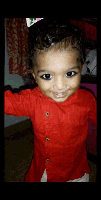 a little girl wearing a red shirt with gold buttons is smiling for the camera