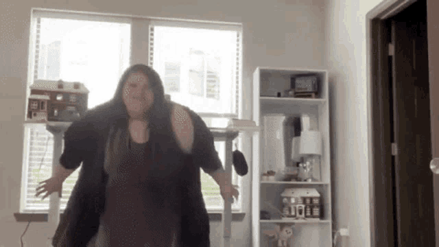 a woman in a purple dress is dancing in front of a window in a living room