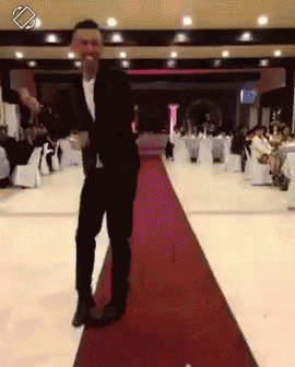 a man in a suit is dancing on a red carpet in a large room