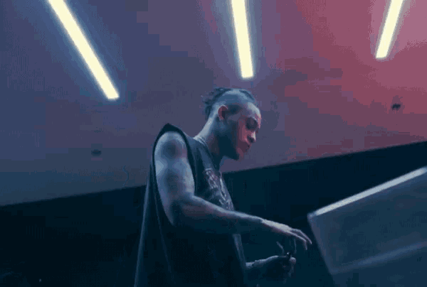 a man in a black tank top is standing in a dark room with a red light behind him