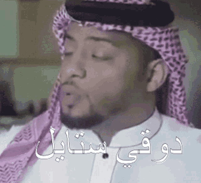 a man wearing a white shirt and a pink scarf has arabic writing on his face .